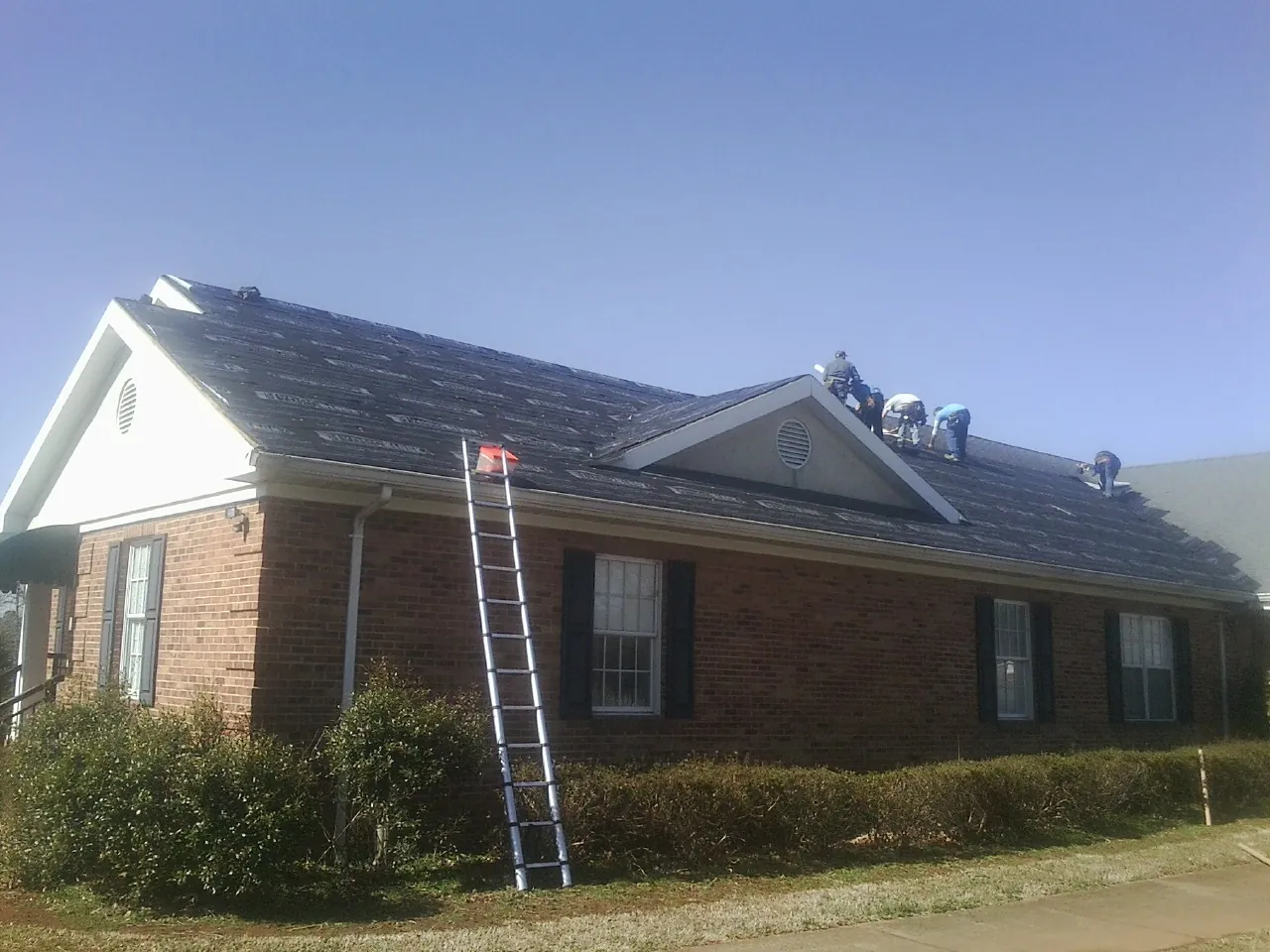 Crew tearing shingles off a brick ranch roof with a ladder set — Emergency Roof Repair work by our crew in Acworth