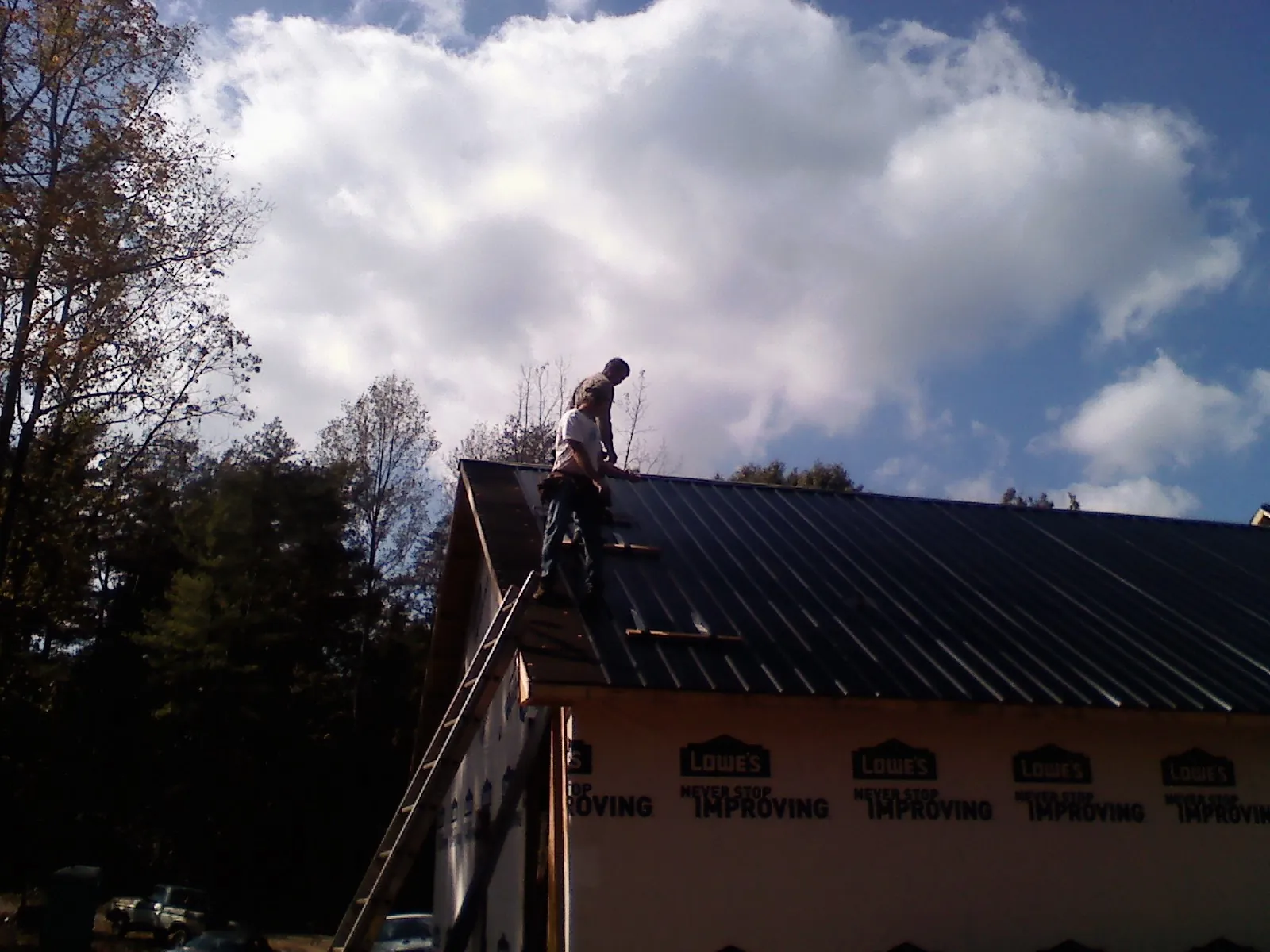 Roofer fastening dark metal panels high against a cloudy sky, from a Roof Inspection job in Acworth